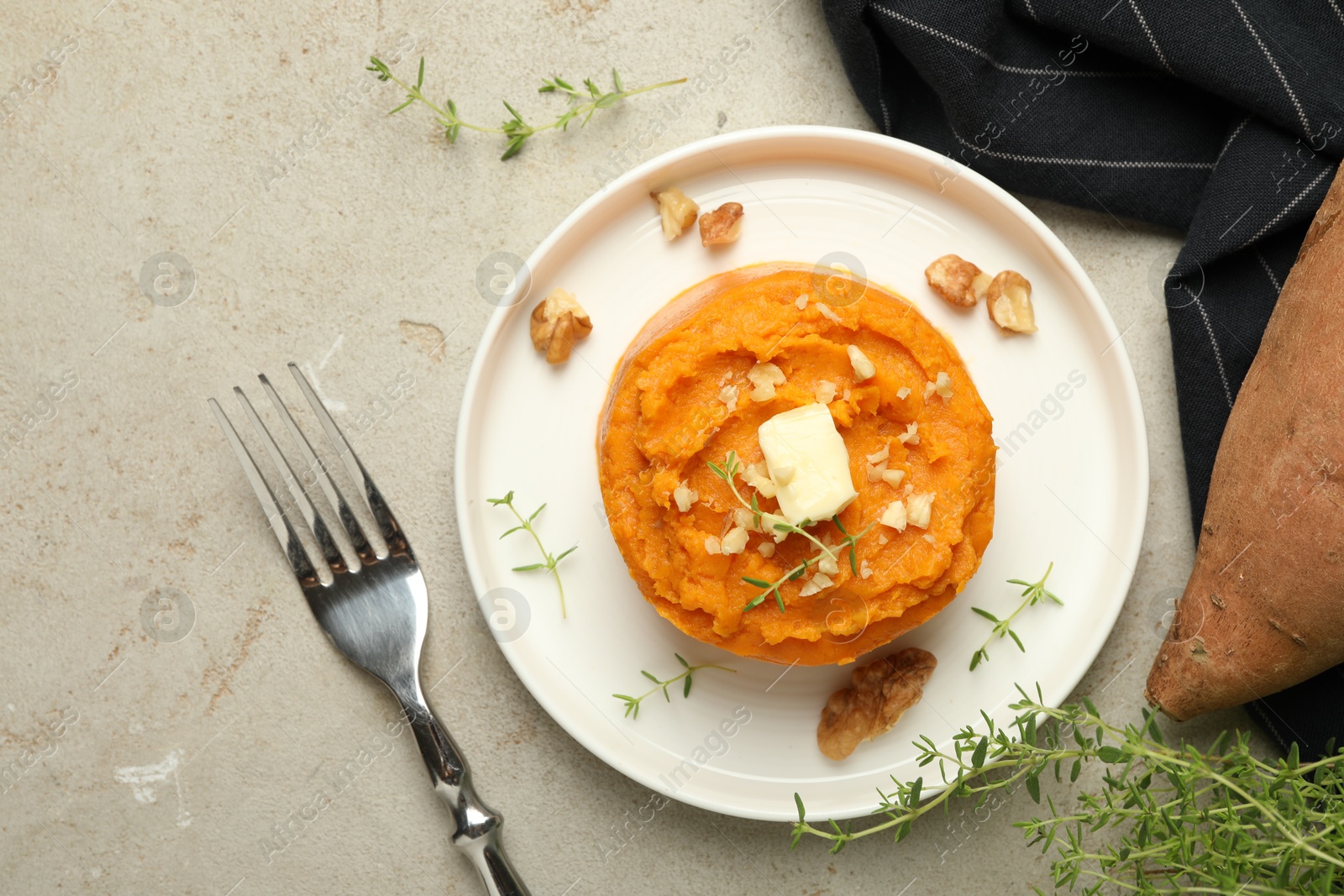 Photo of Tasty mashed sweet potato, butter, thyme and walnuts served on grey textured table, flat lay