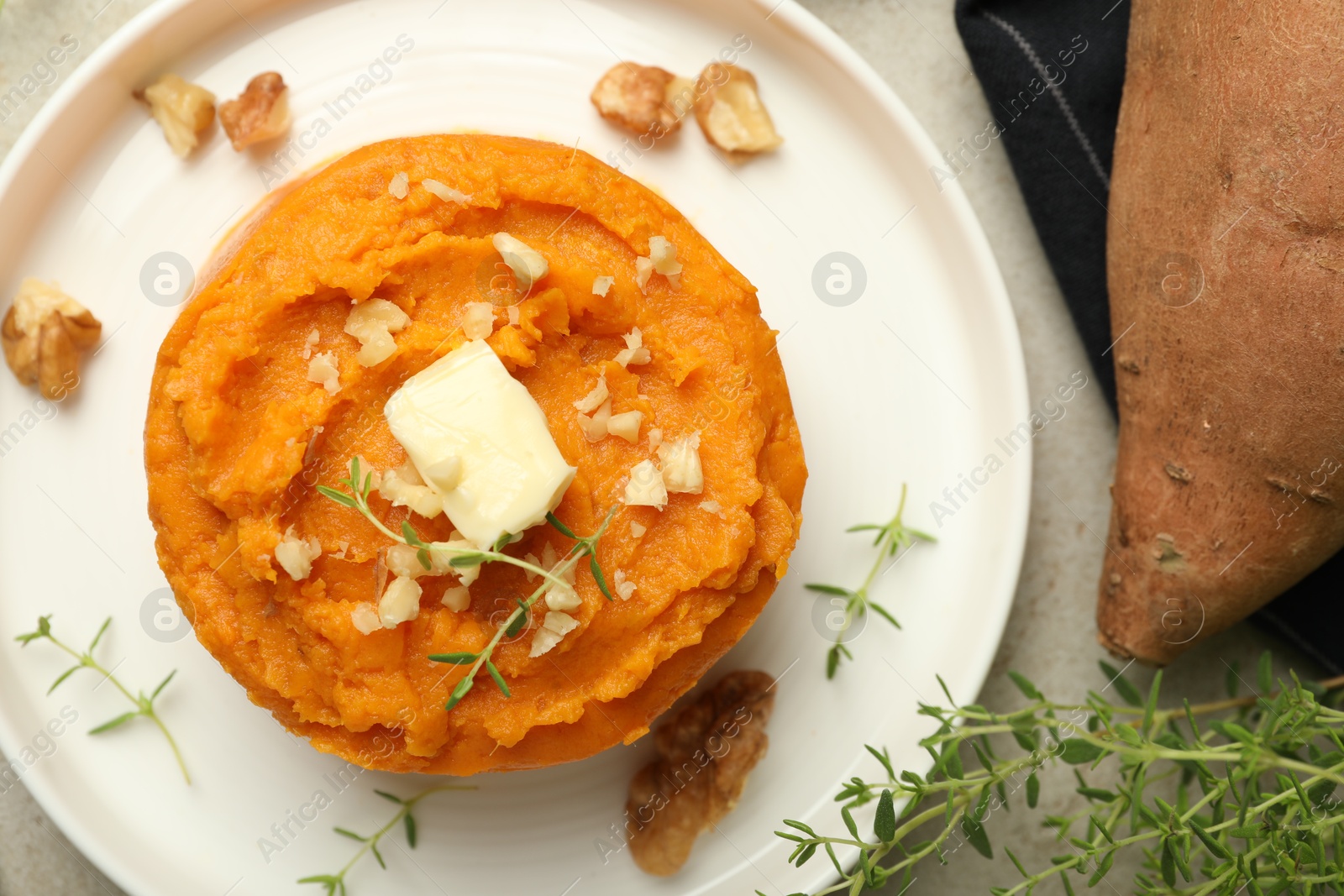 Photo of Tasty mashed sweet potato, butter, thyme and walnuts on grey table, flat lay