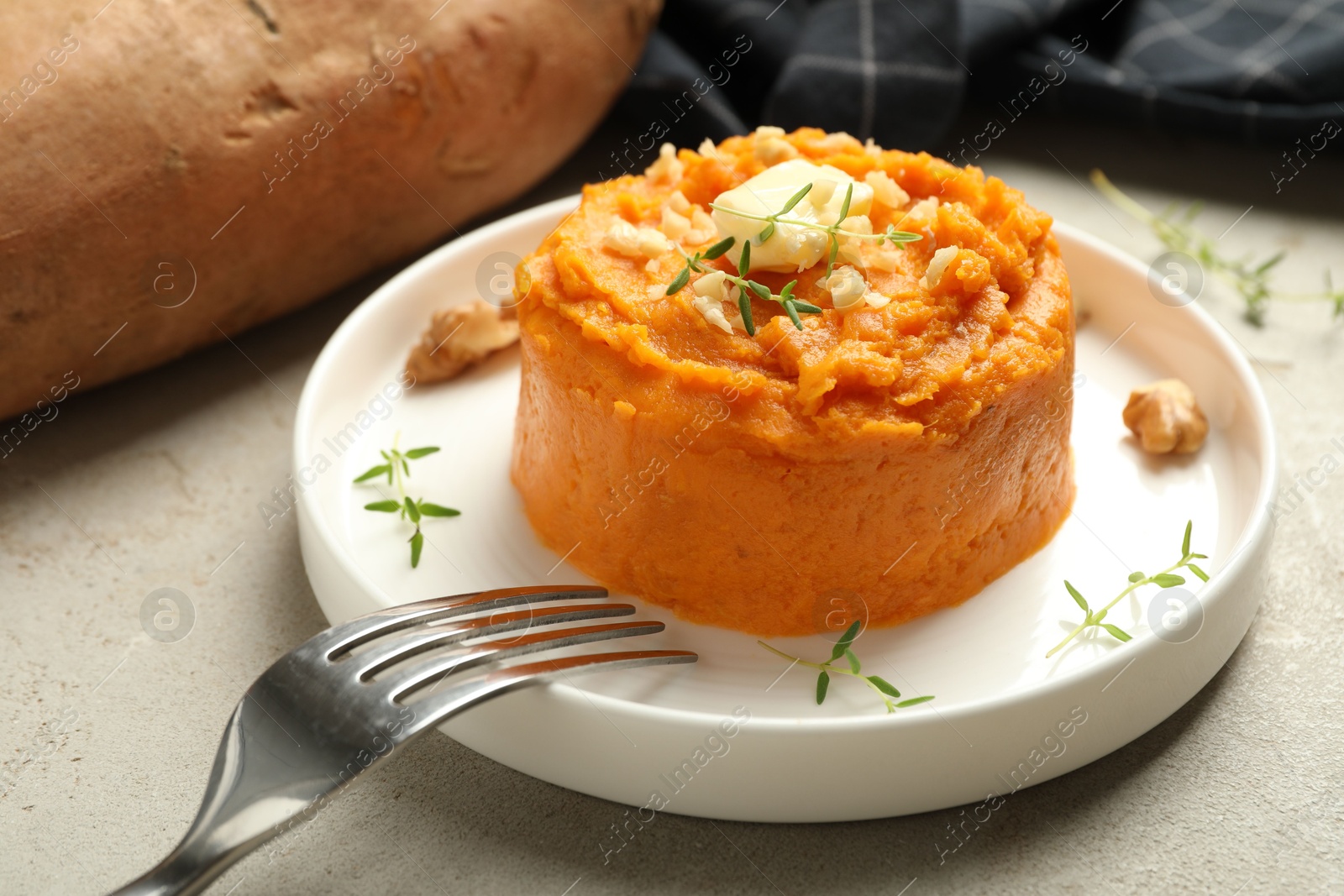 Photo of Plate with tasty mashed sweet potato, butter, thyme and walnuts on grey textured table, closeup