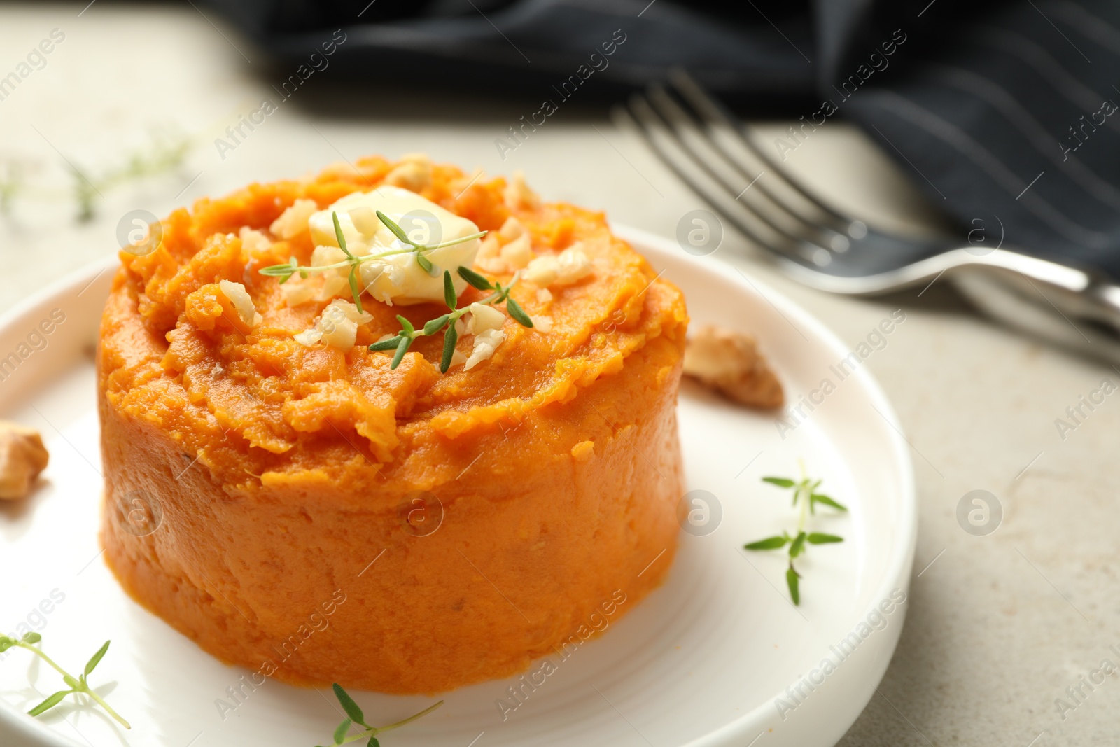 Photo of Plate with tasty mashed sweet potato, butter, thyme and walnuts on grey textured table, closeup