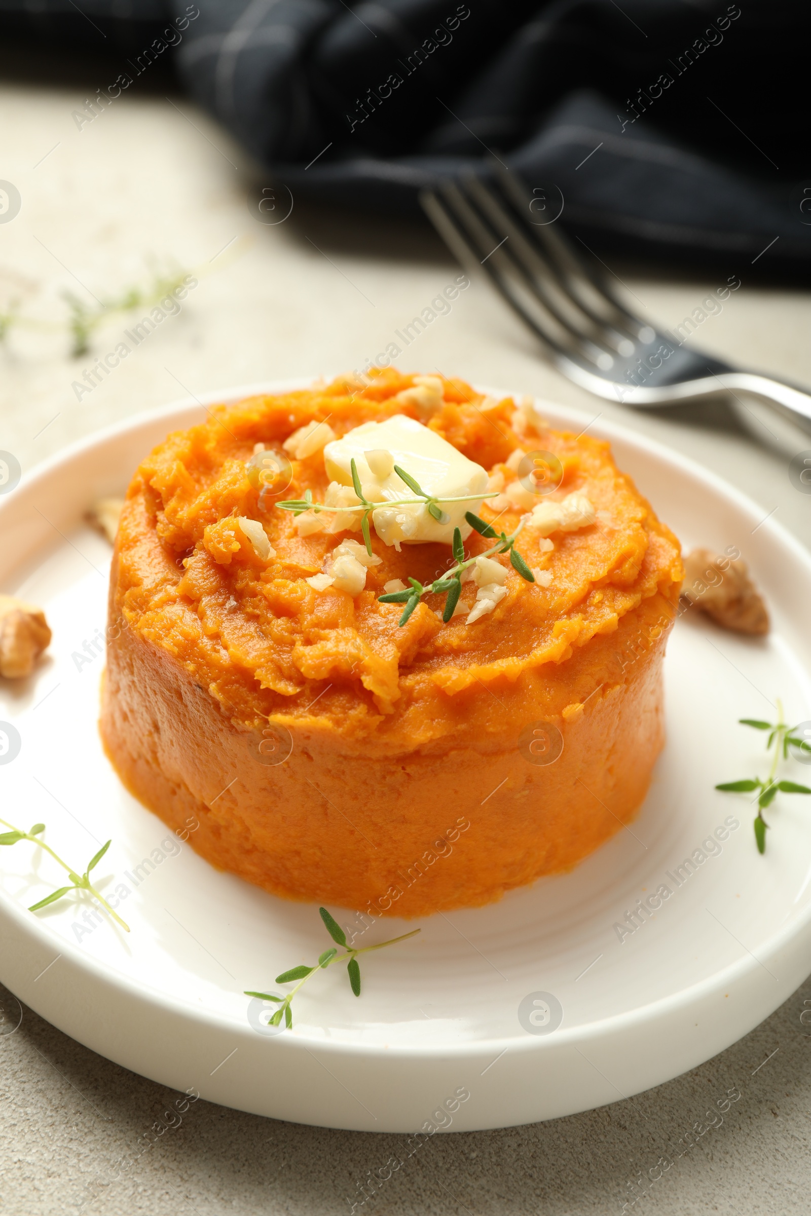 Photo of Plate with tasty mashed sweet potato, butter, thyme and walnuts on grey textured table, closeup