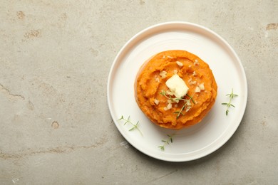 Photo of Plate with tasty mashed sweet potato, butter, thyme and walnuts on grey textured table, top view. Space for text