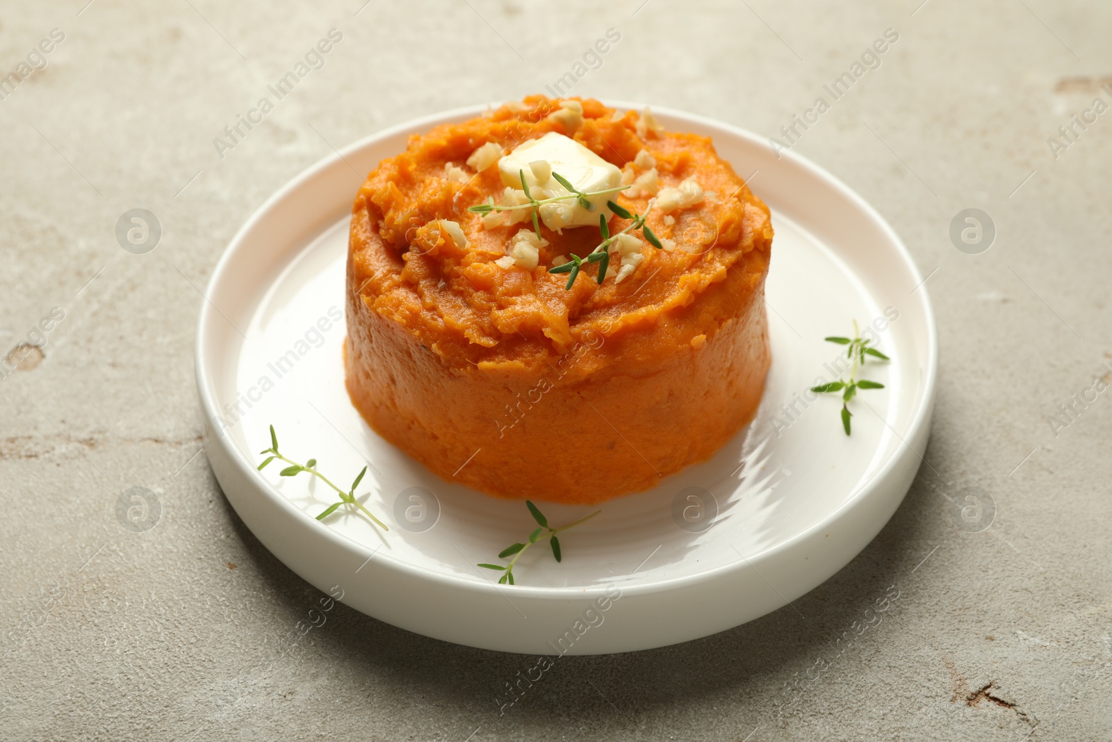 Photo of Plate with tasty mashed sweet potato, butter, thyme and walnuts on grey textured table, closeup