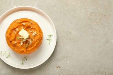 Photo of Plate with tasty mashed sweet potato, butter, thyme and walnuts on grey textured table, top view. Space for text