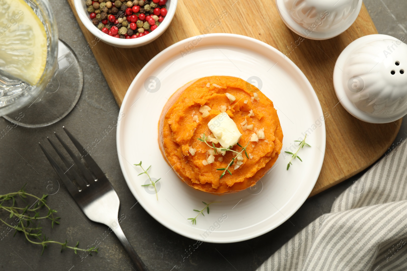 Photo of Tasty mashed sweet potato, butter, thyme and walnuts served on grey textured table, flat lay