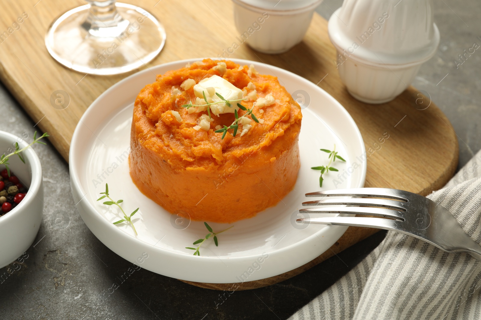 Photo of Plate with tasty mashed sweet potato, butter, thyme and walnuts served on grey textured table, closeup