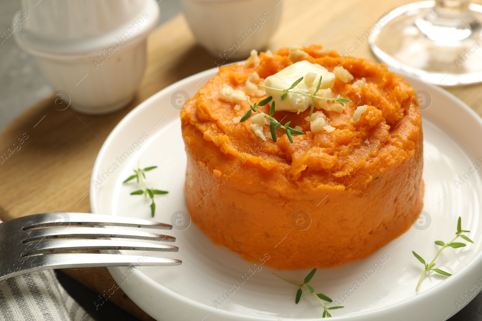 Photo of Plate with tasty mashed sweet potato, butter, thyme and walnuts served on table, closeup