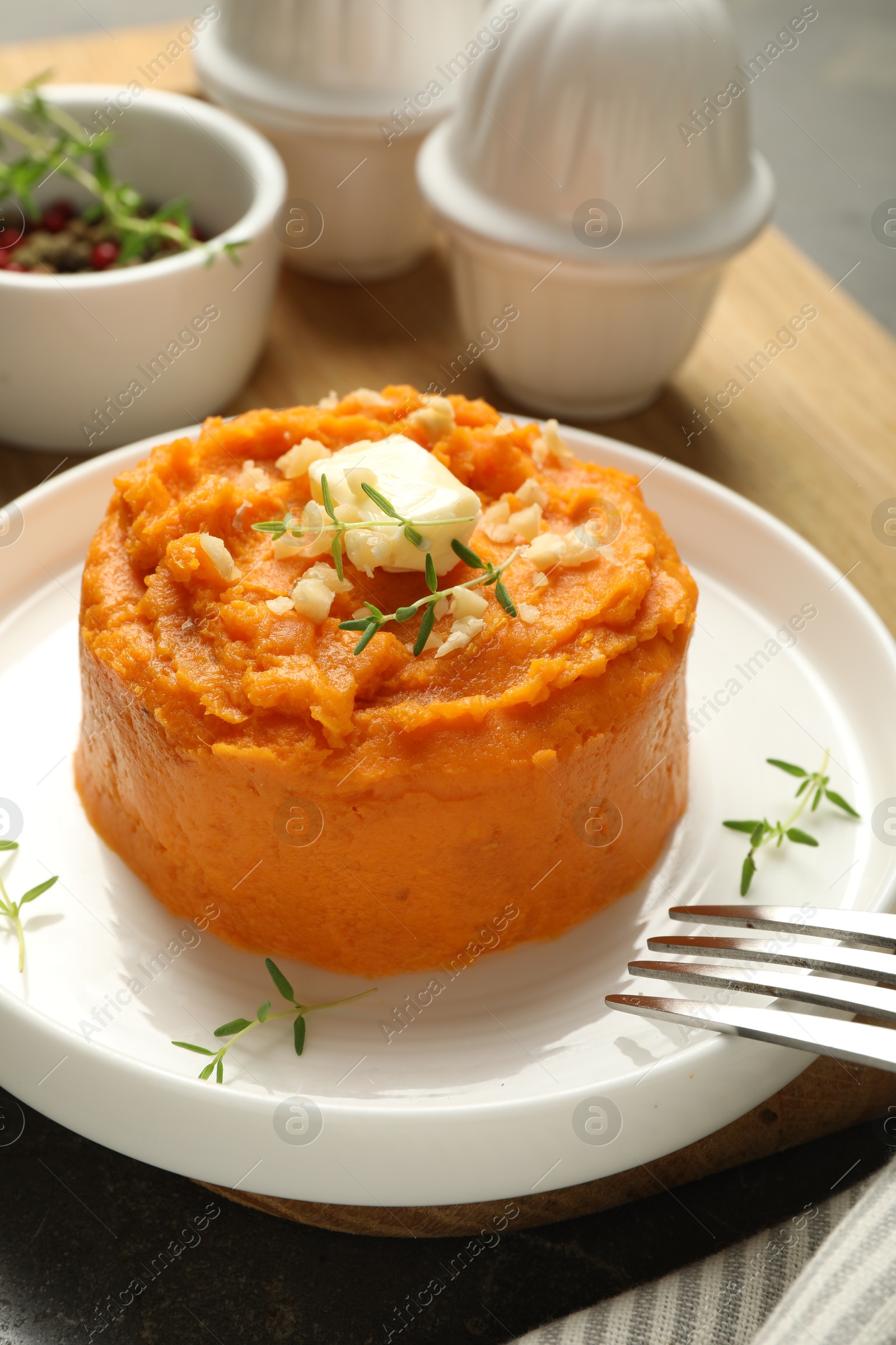 Photo of Plate with tasty mashed sweet potato, butter, thyme and walnuts served on table, closeup