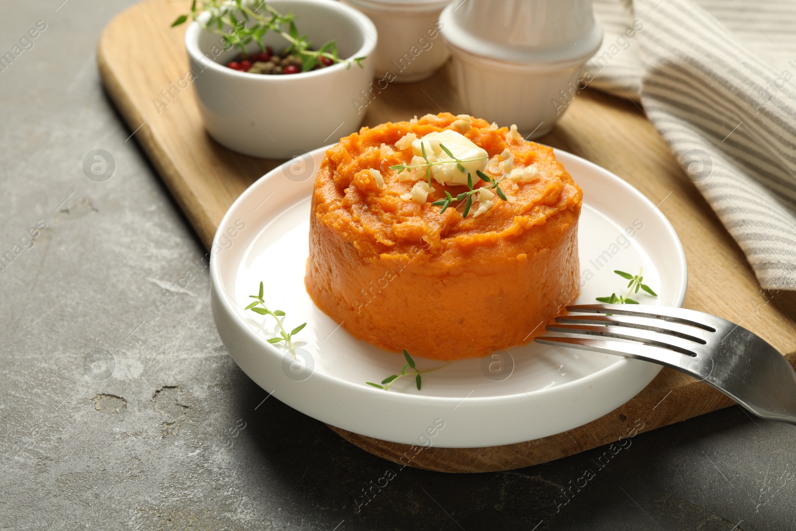 Photo of Plate with tasty mashed sweet potato, butter, thyme and walnuts served on grey textured table, closeup