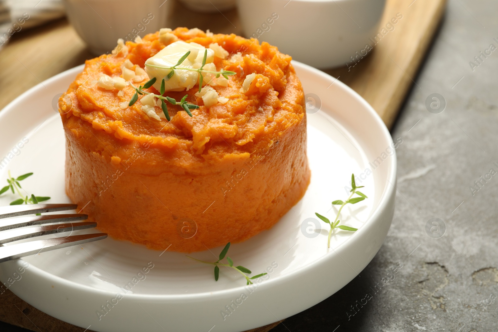 Photo of Plate with tasty mashed sweet potato, butter, thyme and walnuts served on grey textured table, closeup