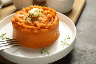 Photo of Plate with tasty mashed sweet potato, butter, thyme and walnuts served on grey textured table, closeup