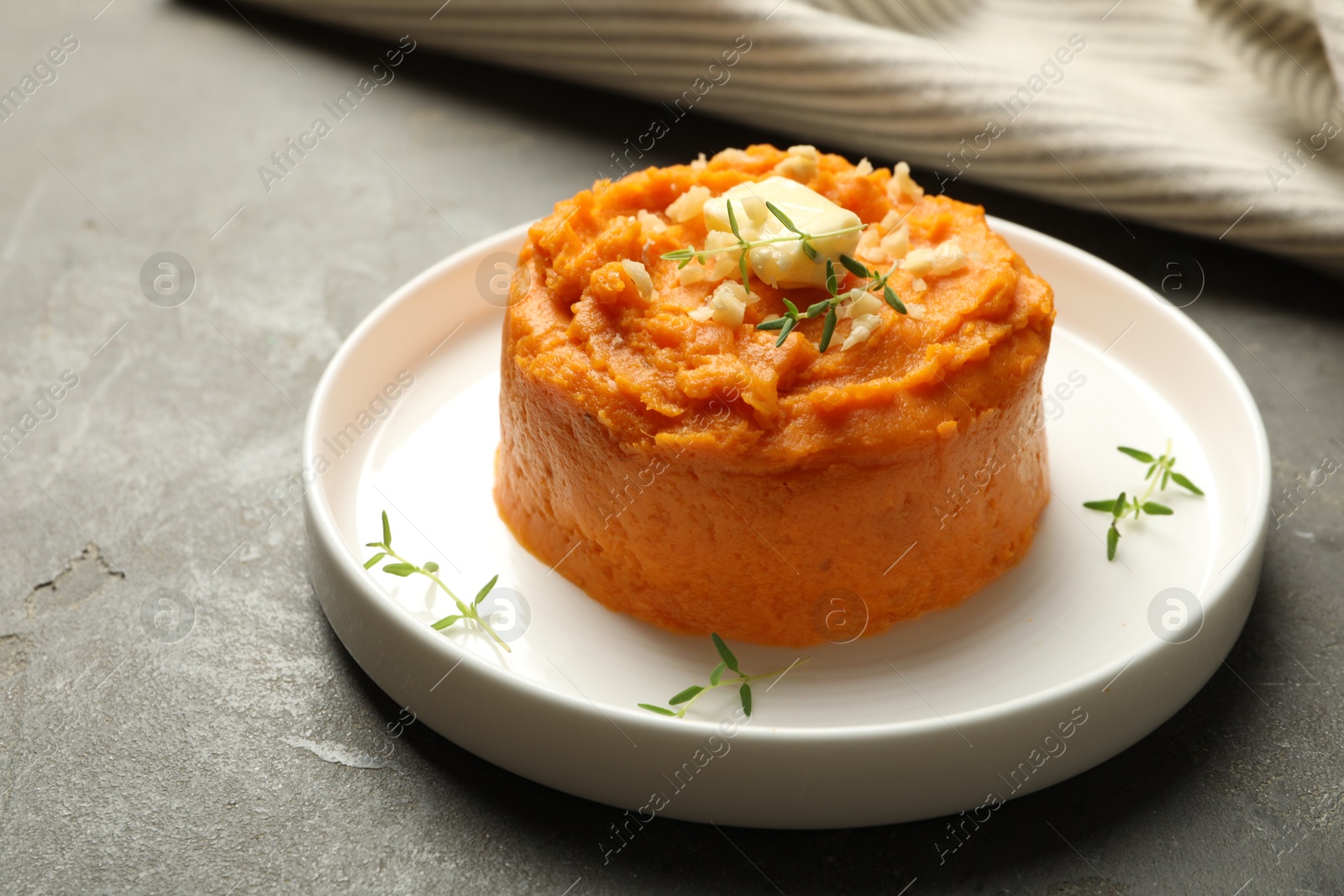 Photo of Plate with tasty mashed sweet potato, butter, thyme and walnuts on grey textured table, closeup