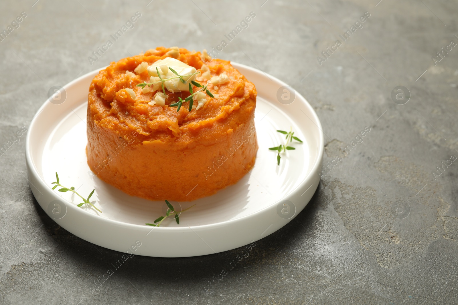 Photo of Plate with tasty mashed sweet potato, butter, thyme and walnuts on grey textured table, closeup. Space for text