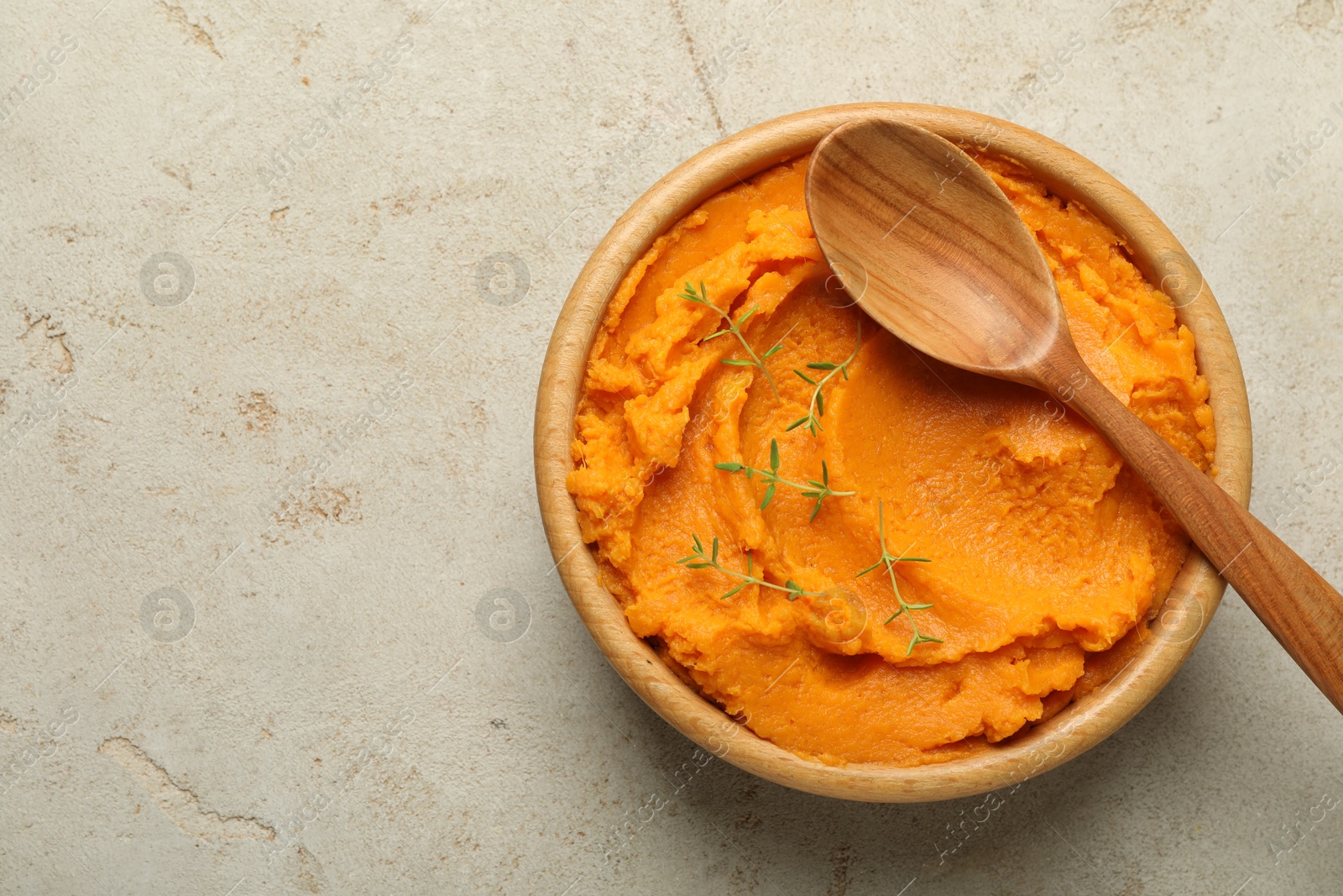 Photo of Tasty mashed sweet potato and thyme in bowl on grey textured table, top view. Space for text