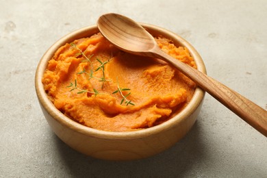 Photo of Tasty mashed sweet potato and thyme in bowl on grey textured table, closeup