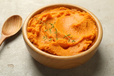 Photo of Tasty mashed sweet potato and thyme in bowl on grey textured table, closeup