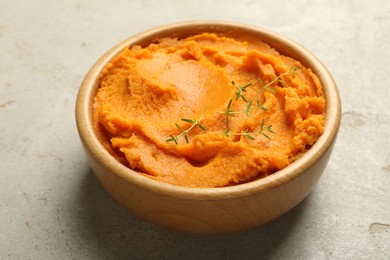 Photo of Tasty mashed sweet potato and thyme in bowl on grey textured table, closeup