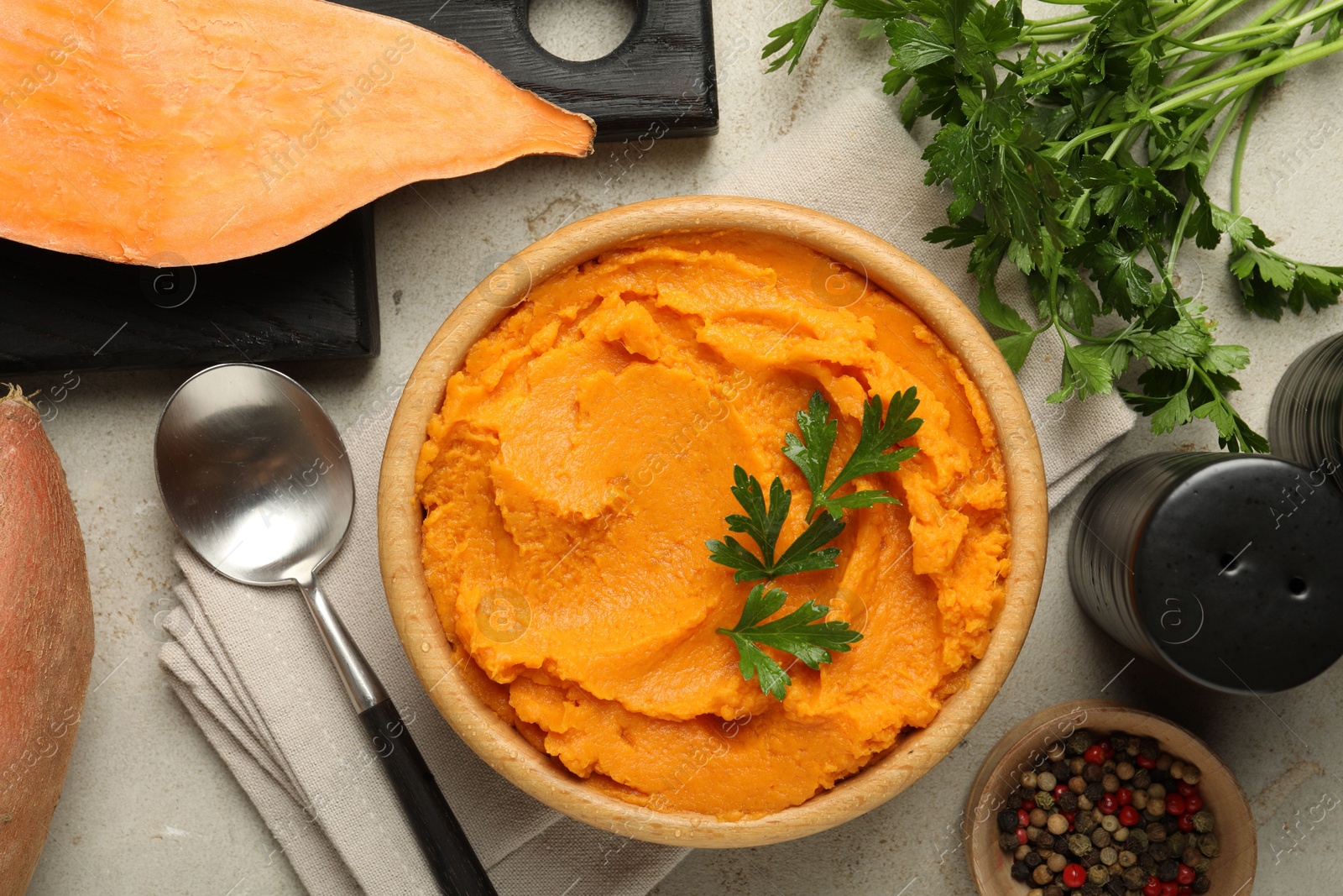 Photo of Tasty mashed sweet potato and parsley in bowl served on grey textured table, flat lay