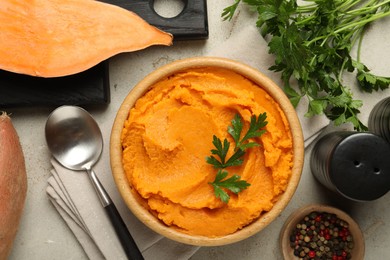 Photo of Tasty mashed sweet potato and parsley in bowl served on grey textured table, flat lay