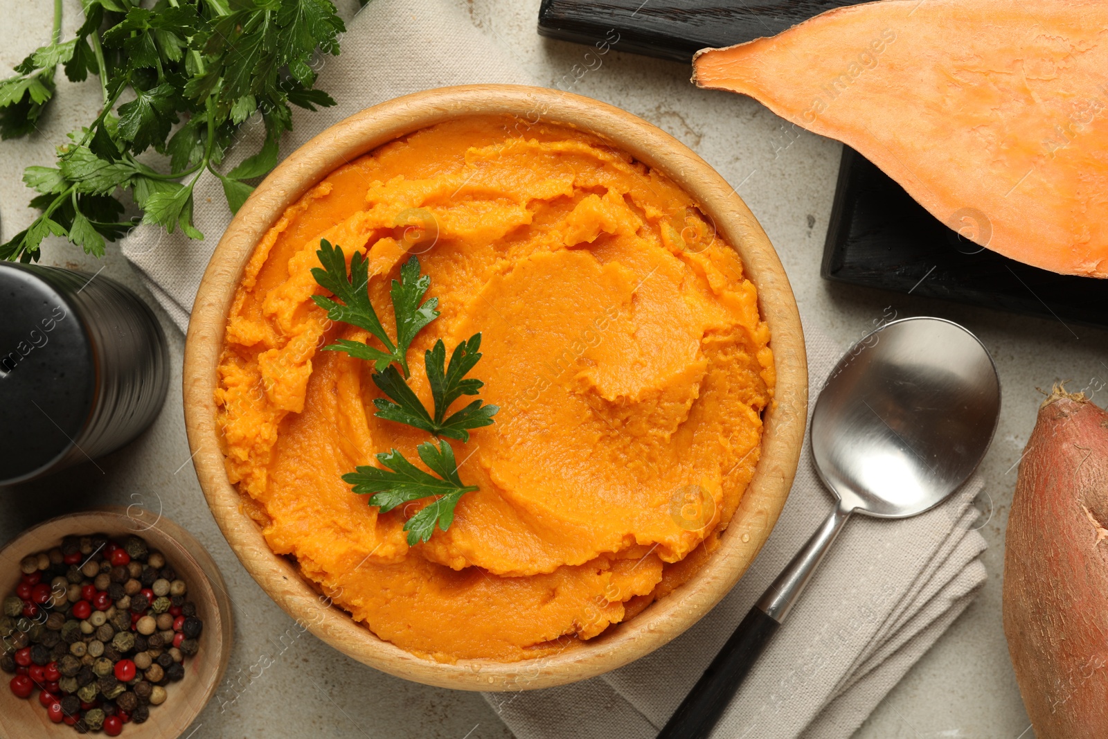 Photo of Tasty mashed sweet potato and parsley in bowl served on grey textured table, flat lay