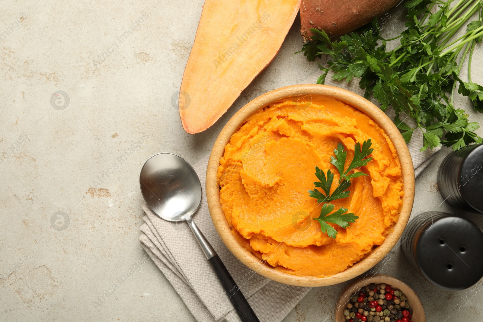 Photo of Tasty mashed sweet potato and parsley in bowl served on grey textured table, flat lay. Space for text