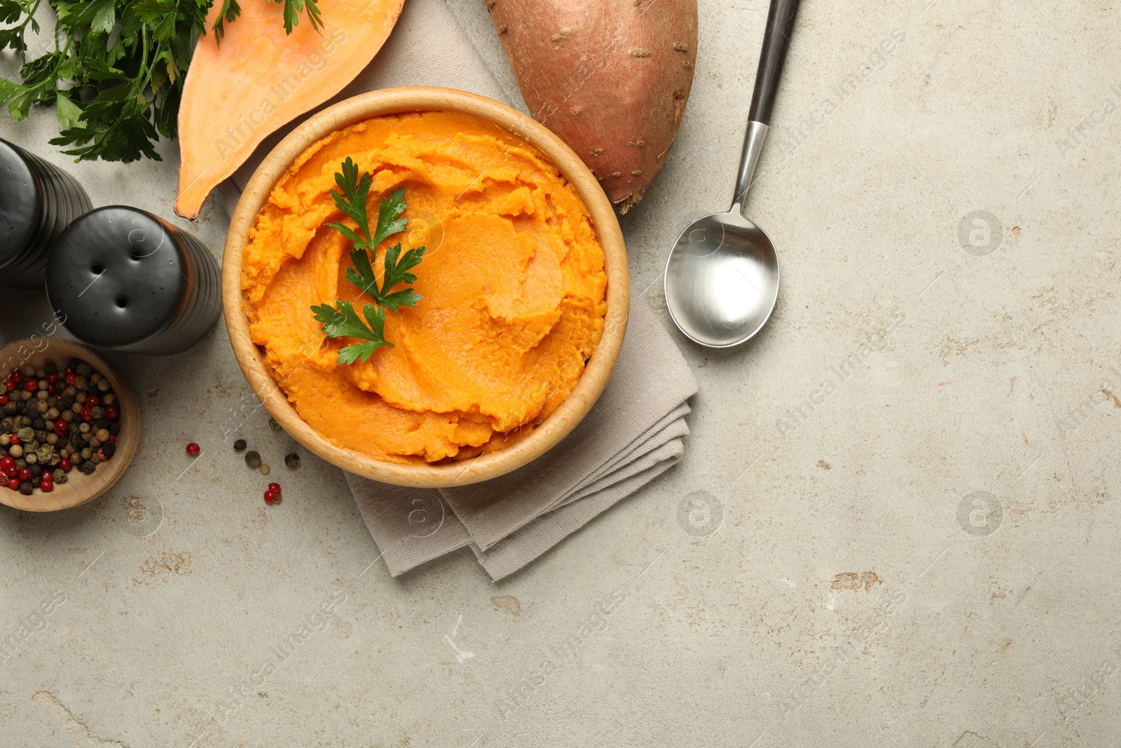 Photo of Tasty mashed sweet potato and parsley in bowl served on grey textured table, flat lay. Space for text