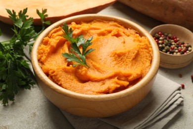 Photo of Tasty mashed sweet potato and parsley in bowl on grey textured table, closeup