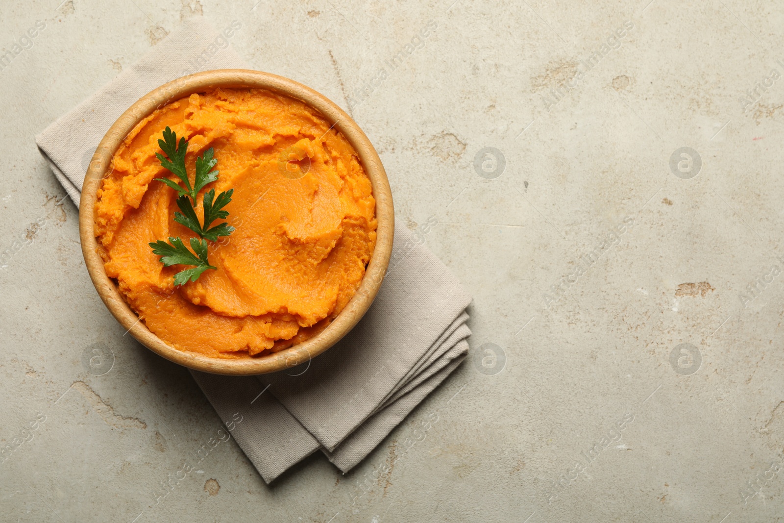 Photo of Tasty mashed sweet potato and parsley in bowl on grey textured table, top view. Space for text