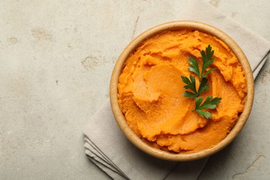 Photo of Tasty mashed sweet potato and parsley in bowl on grey textured table, top view. Space for text