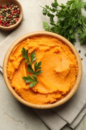 Photo of Tasty mashed sweet potato and parsley in bowl on grey textured table, flat lay