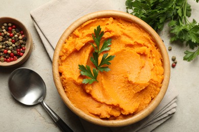 Photo of Tasty mashed sweet potato and parsley in bowl served on grey textured table, flat lay