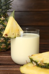 Photo of Tasty pineapple smoothie in glass and slices of fruit on wooden table, closeup