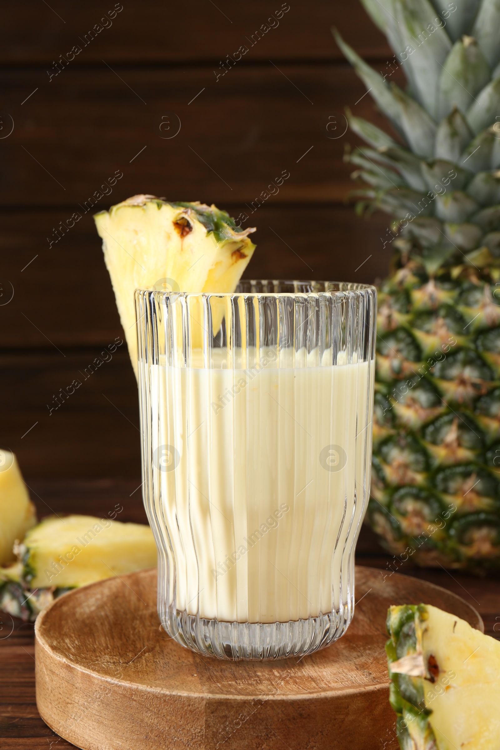 Photo of Tasty pineapple smoothie in glass and slices of fruit on wooden table, closeup