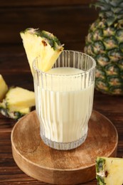 Photo of Tasty pineapple smoothie in glass and slices of fruit on wooden table, closeup