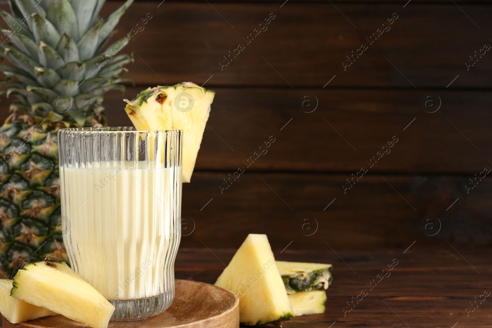 Photo of Tasty pineapple smoothie in glass and slices of fruit on wooden table, closeup. Space for text