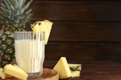 Photo of Tasty pineapple smoothie in glass and slices of fruit on wooden table, closeup. Space for text