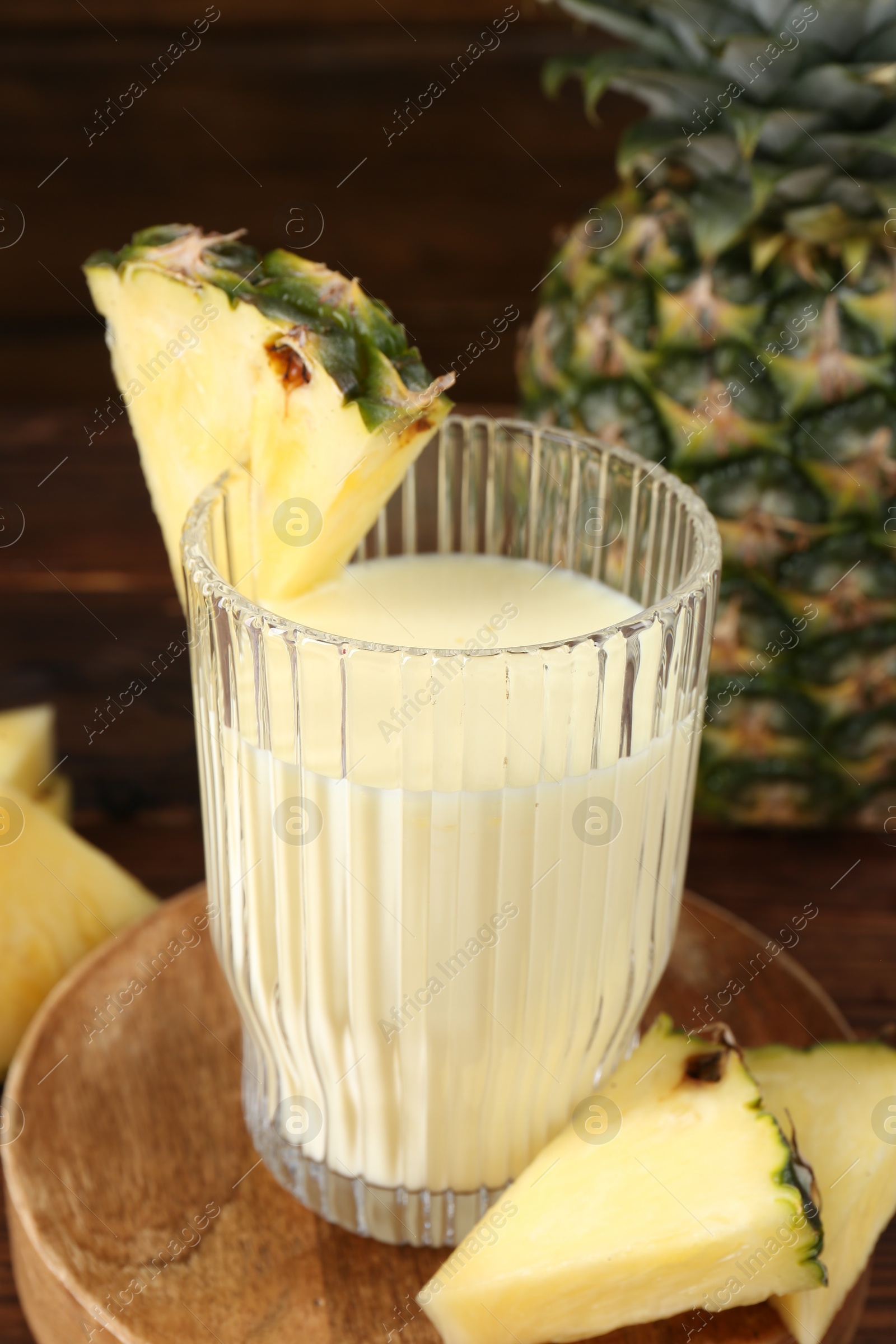 Photo of Tasty pineapple smoothie in glass and slices of fruit on wooden table, closeup