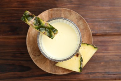 Photo of Tasty pineapple smoothie in glass and slices of fruit on wooden table, top view