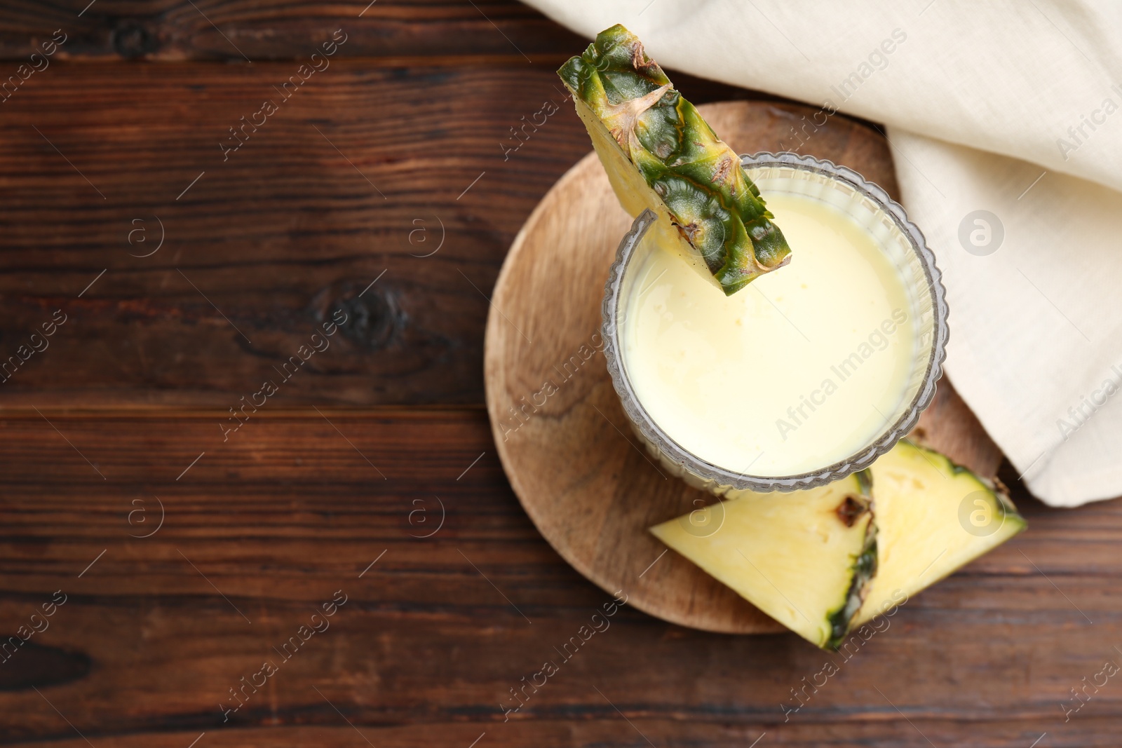 Photo of Tasty pineapple smoothie in glass and slices of fruit on wooden table, top view. Space for text