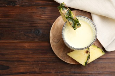 Photo of Tasty pineapple smoothie in glass and slices of fruit on wooden table, top view. Space for text