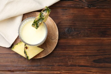 Photo of Tasty pineapple smoothie in glass and slices of fruit on wooden table, top view. Space for text