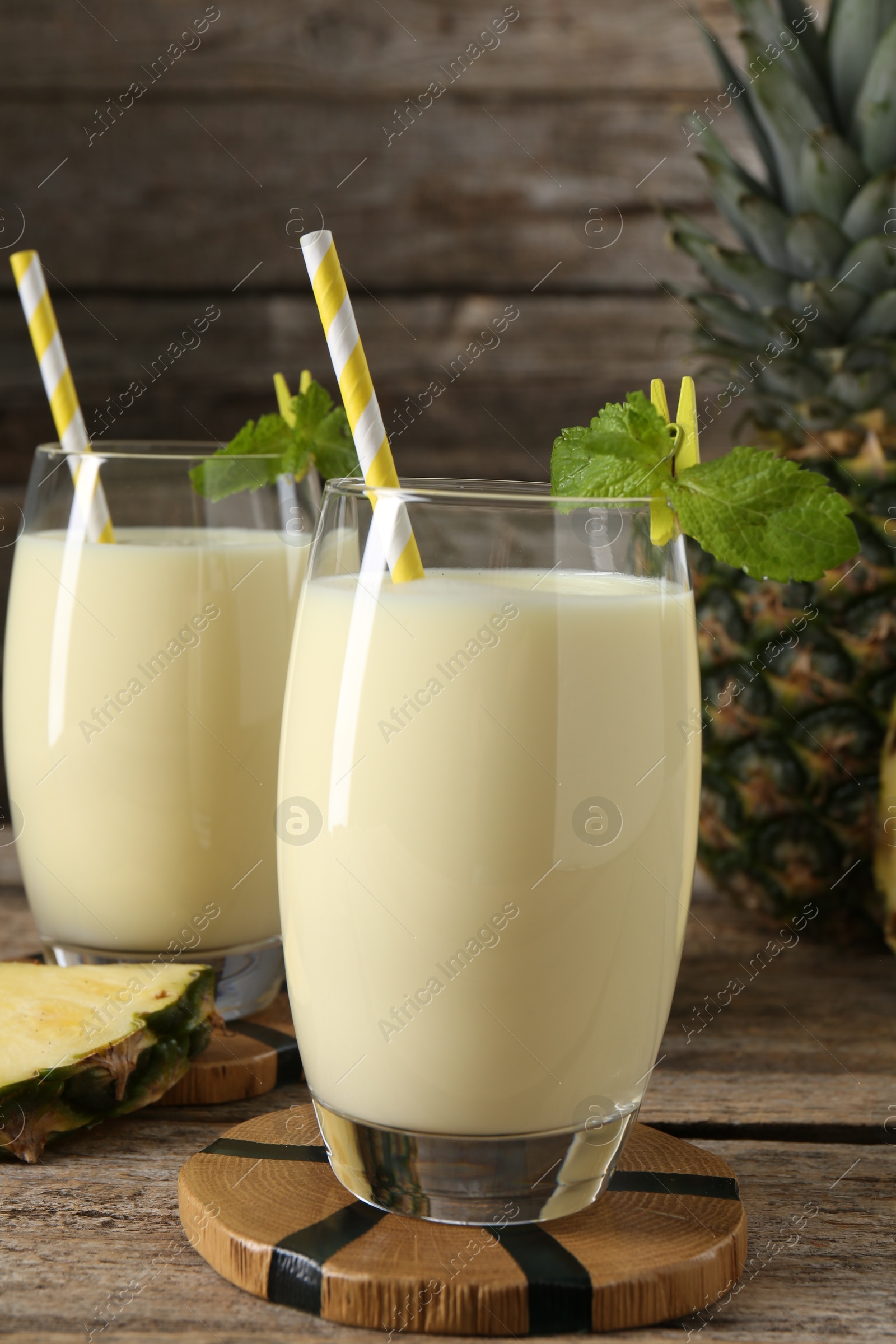 Photo of Tasty pineapple smoothie in glasses, mint and fruit on wooden table, closeup