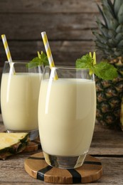 Photo of Tasty pineapple smoothie in glasses, mint and fruit on wooden table, closeup