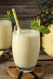 Photo of Tasty pineapple smoothie in glasses, mint and fruit on wooden table, closeup