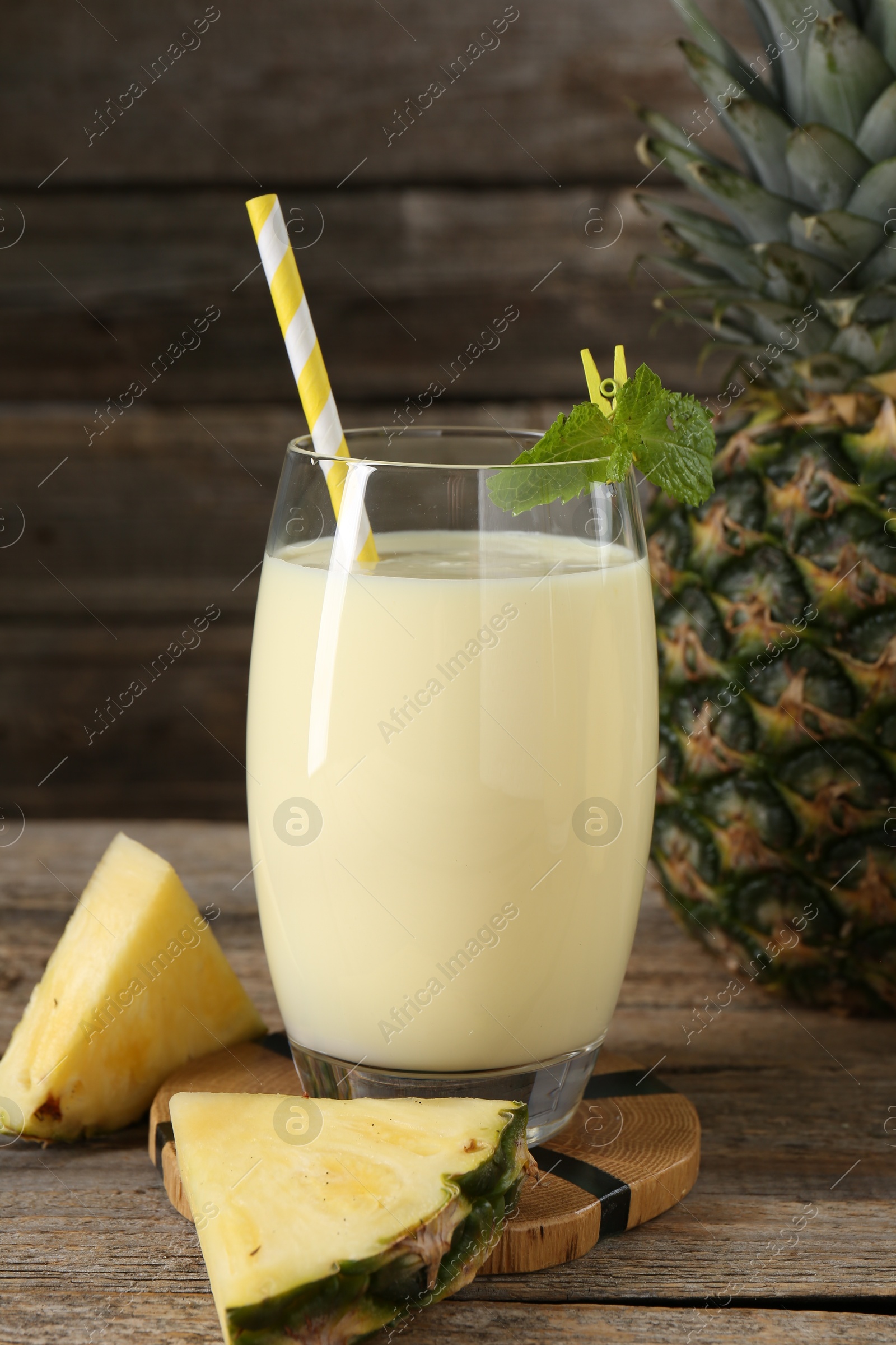 Photo of Tasty pineapple smoothie in glass, mint and fruit on wooden table, closeup