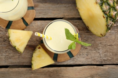 Photo of Tasty pineapple smoothie in glass, mint and slices of fruit on wooden table, flat lay