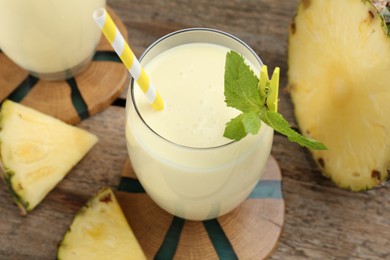 Photo of Tasty pineapple smoothie in glass, mint and slices of fruit on wooden table, closeup