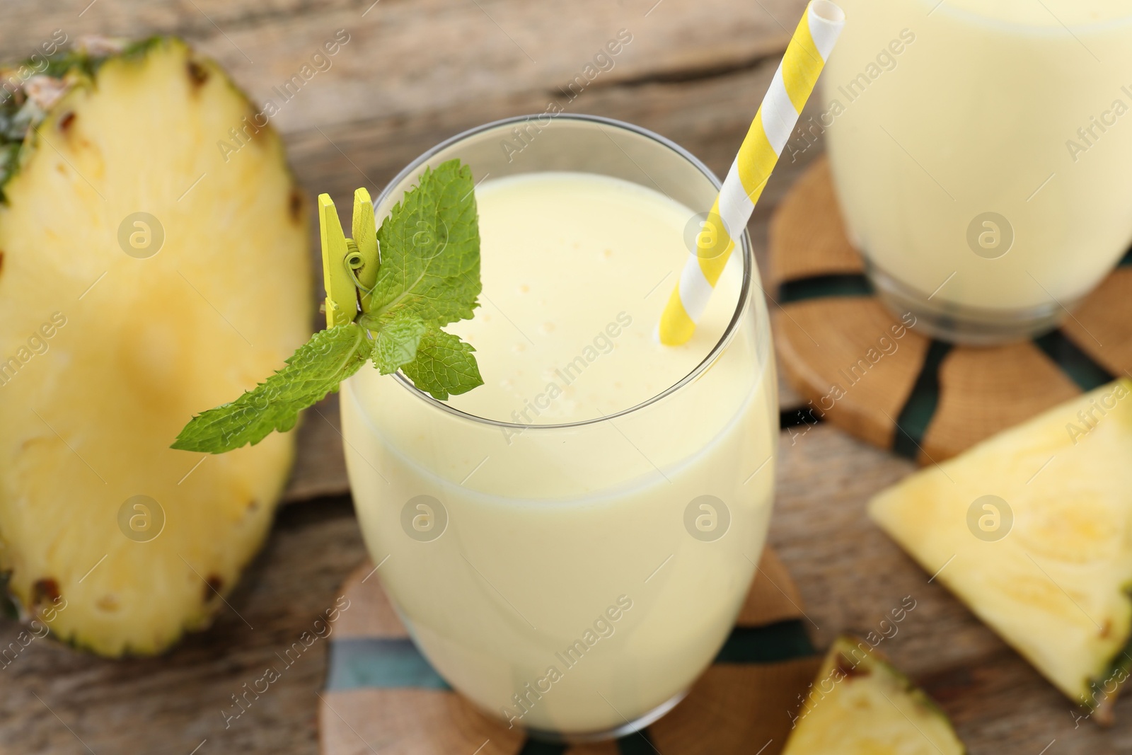 Photo of Tasty pineapple smoothie in glass, mint and slices of fruit on wooden table, closeup