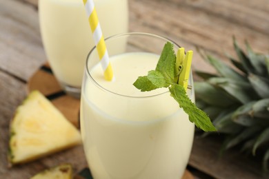 Photo of Tasty pineapple smoothie in glass, mint and slices of fruit on wooden table, closeup