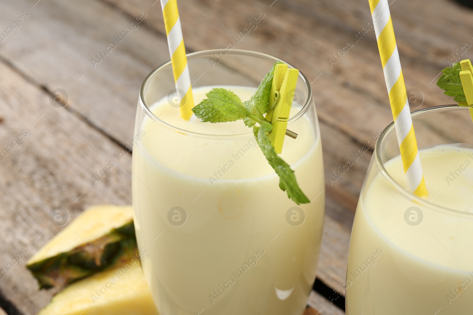 Photo of Tasty pineapple smoothie in glasses, mint and slices of fruit on wooden table, closeup